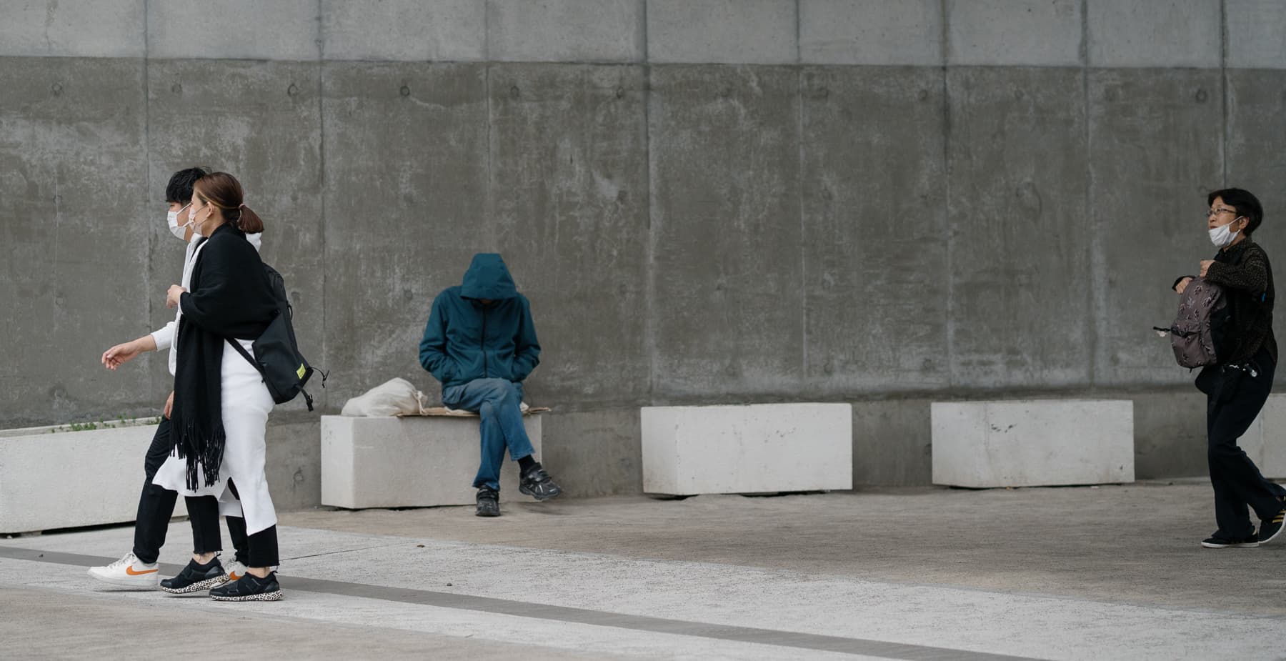 A man sitting alone with his face covered by a hooded jacket.